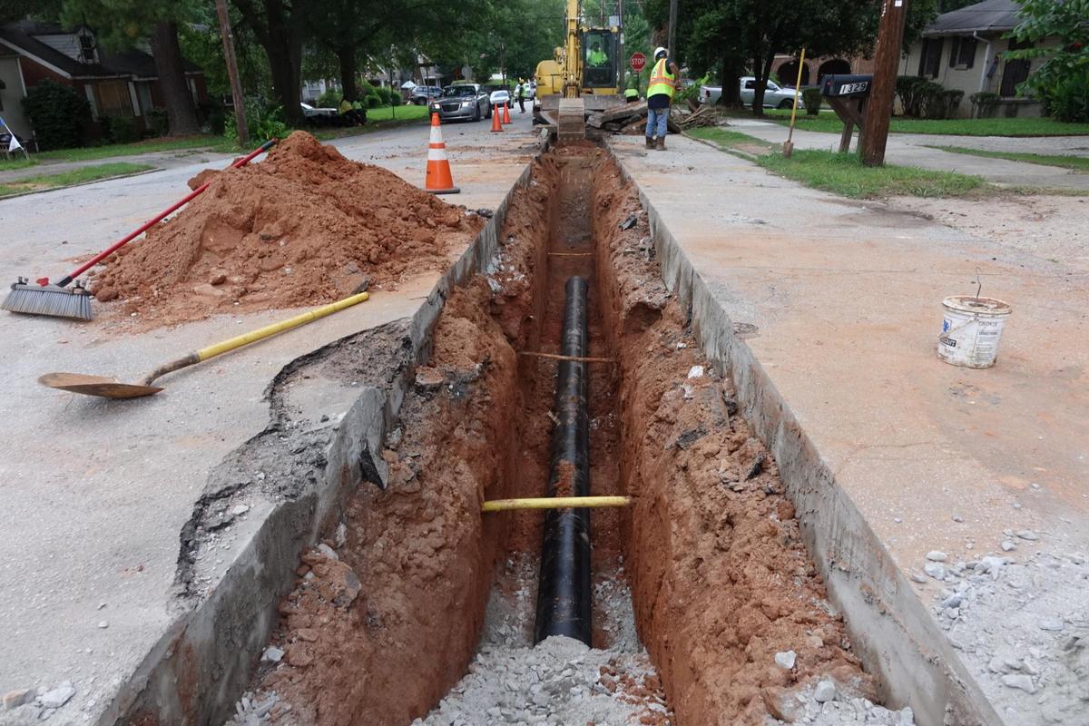 Shored trench across a residential street with new HDPE main and gravel bedding
