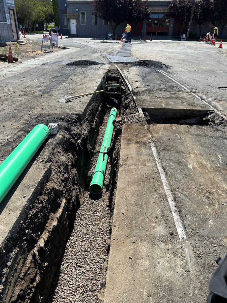 Commercial street trench with green SDR-35 sewer pipe staged and laid