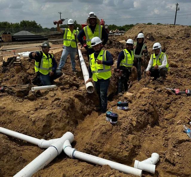 Viper crew in hard hats and hi-vis vests standing in a large trench with PVC mains